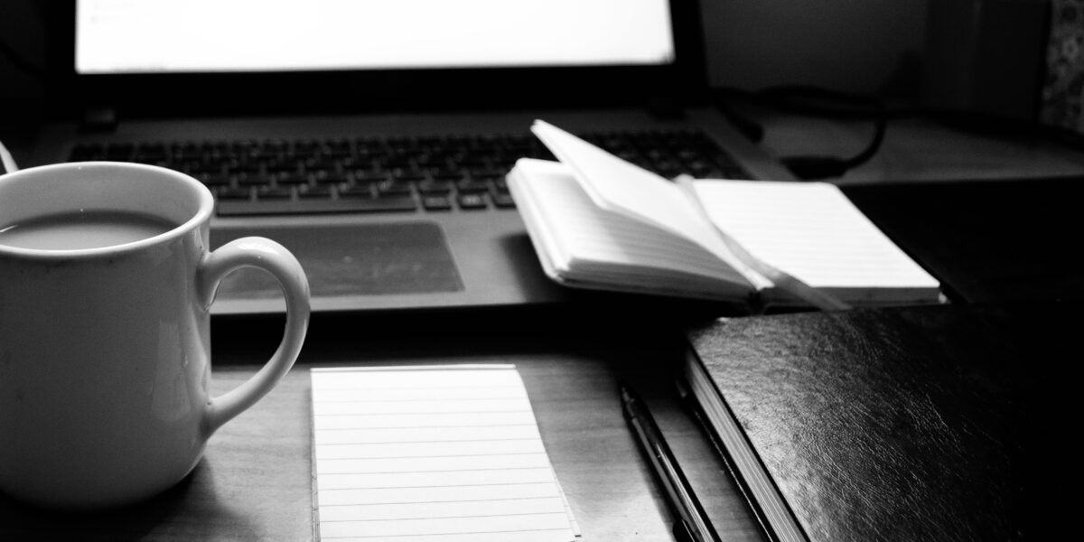Notebook, coffee and laptop on a desk, representing thoughtful business communication and writing.